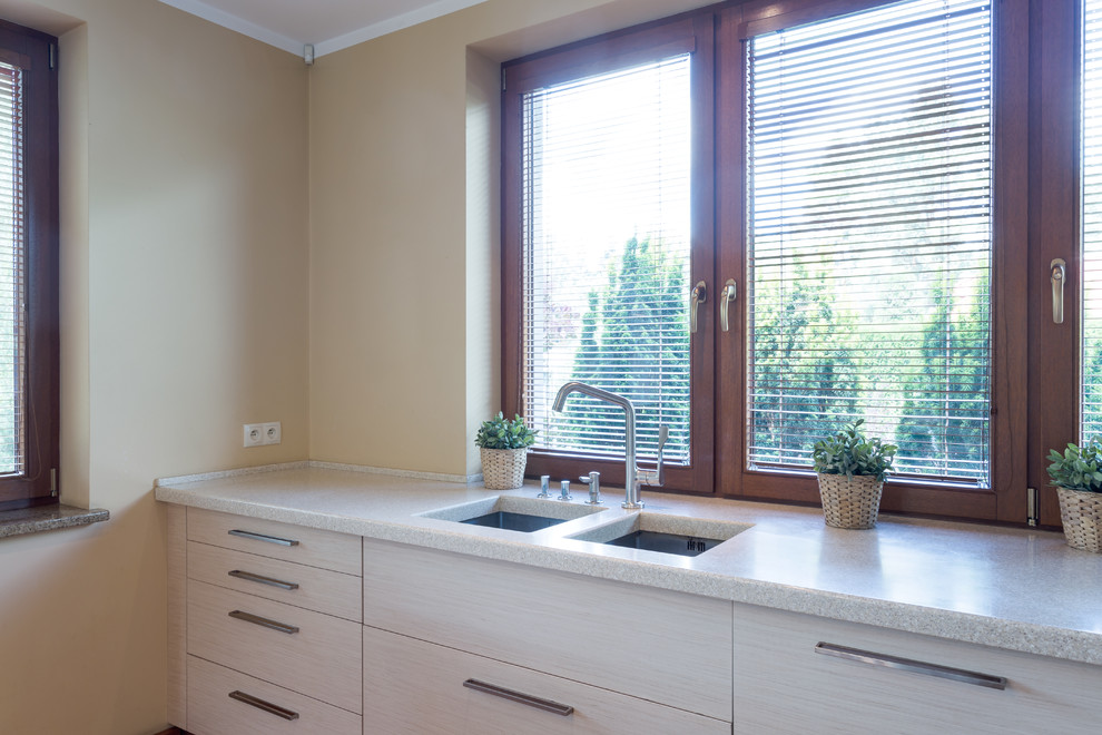 Modern inredning av ett mellanstort linjärt kök och matrum, med en undermonterad diskho, släta luckor, skåp i ljust trä, bänkskiva i kalksten, brunt stänkskydd, fönster som stänkskydd och rostfria vitvaror