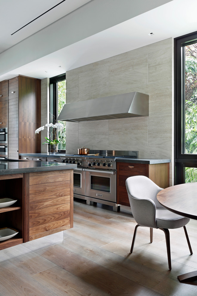 Große Moderne Wohnküche mit flächenbündigen Schrankfronten, dunklen Holzschränken, Küchenrückwand in Grau, Küchengeräten aus Edelstahl, hellem Holzboden und Kücheninsel in Miami
