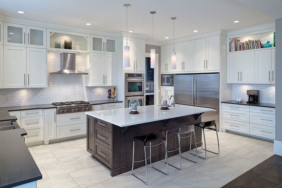Eat-in kitchen - large transitional u-shaped ceramic tile eat-in kitchen idea in Vancouver with a double-bowl sink, shaker cabinets, white cabinets, solid surface countertops, white backsplash, ceramic backsplash, stainless steel appliances and an island