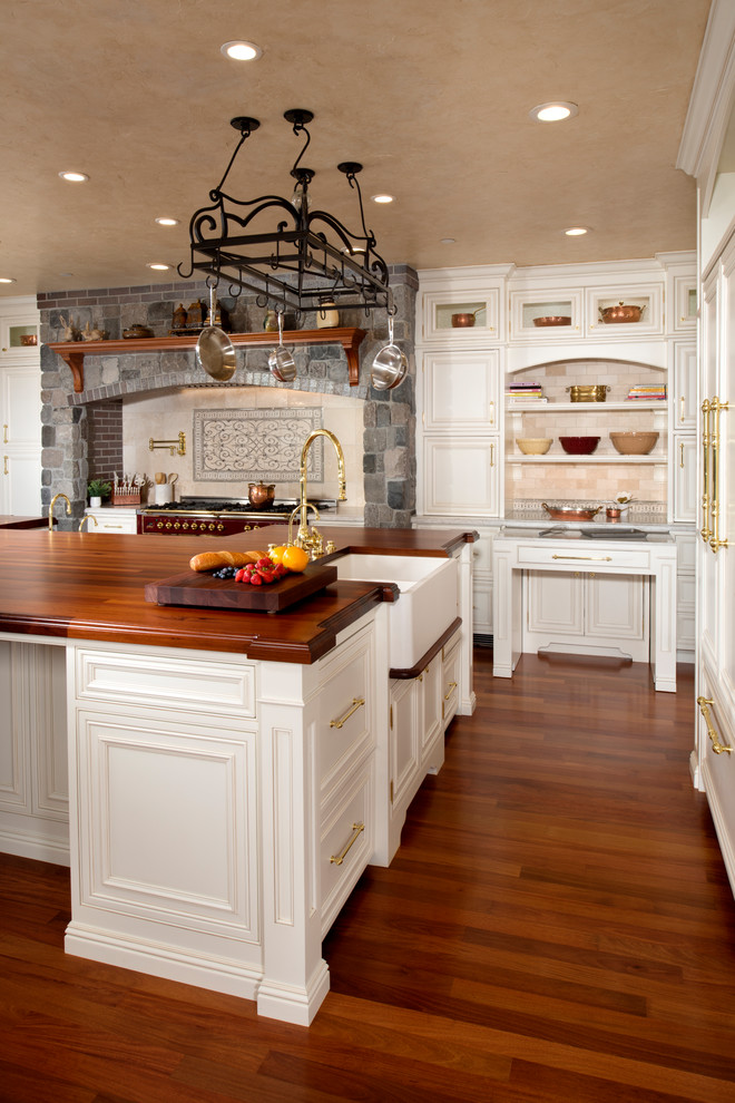 サンフランシスコにあるラグジュアリーな巨大なトラディショナルスタイルのおしゃれなキッチン (エプロンフロントシンク、インセット扉のキャビネット、白いキャビネット、木材カウンター、白いキッチンパネル、トラバーチンのキッチンパネル、パネルと同色の調理設備、濃色無垢フローリング、茶色い床、茶色いキッチンカウンター) の写真