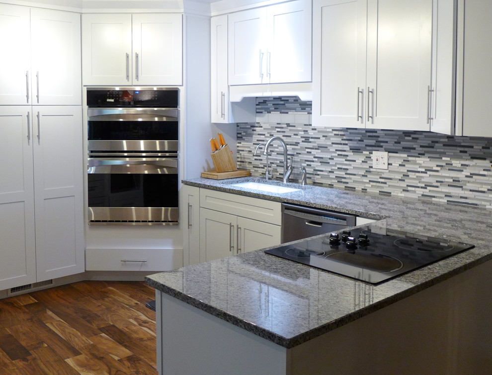 Bild på ett mellanstort funkis kök, med en undermonterad diskho, skåp i shakerstil, vita skåp, granitbänkskiva, grått stänkskydd, stänkskydd i stickkakel, rostfria vitvaror, ljust trägolv, en halv köksö och brunt golv