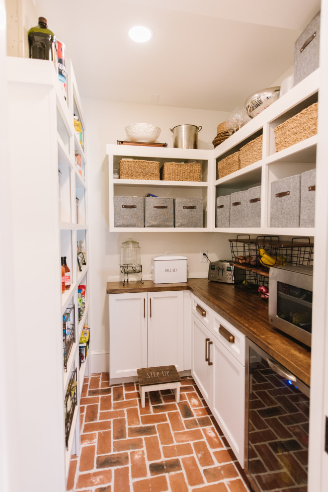 Modelo de cocina ecléctica pequeña con despensa, armarios abiertos, puertas de armario blancas, encimera de madera, electrodomésticos de acero inoxidable, suelo de ladrillo y encimeras marrones