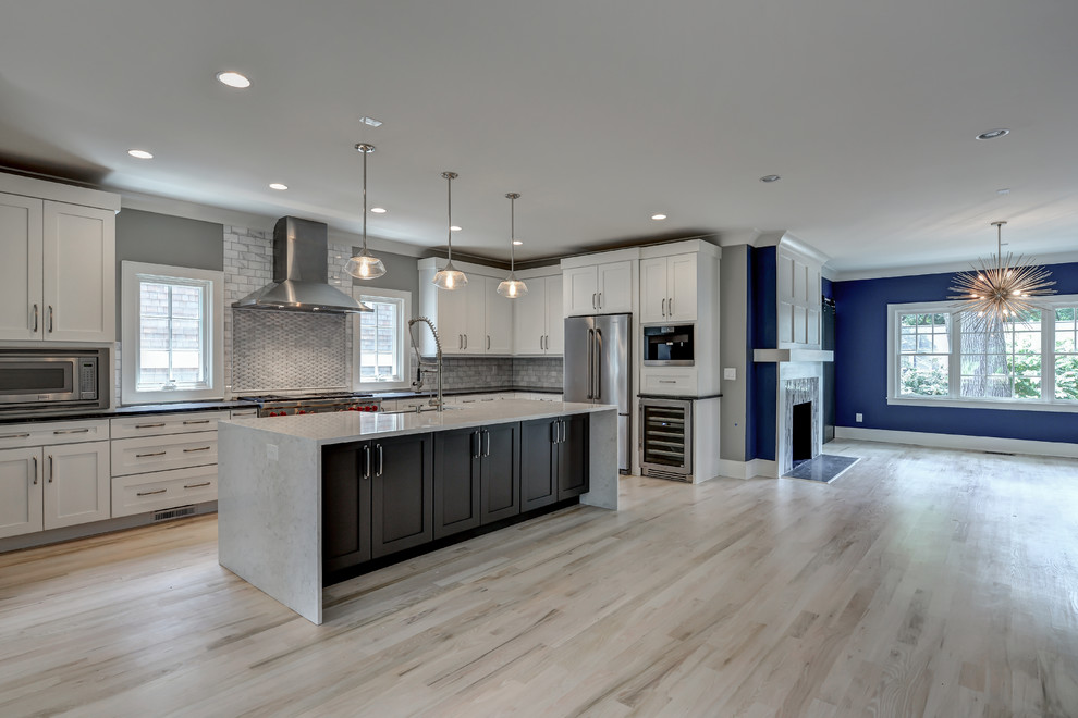 This is an example of a large contemporary l-shaped kitchen in Atlanta with a belfast sink, shaker cabinets, white cabinets, soapstone worktops, grey splashback, stone tiled splashback, stainless steel appliances, light hardwood flooring and an island.