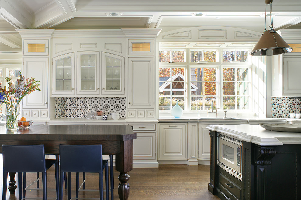 Klassisk inredning av ett stort kök, med en undermonterad diskho, luckor med upphöjd panel, vita skåp, flerfärgad stänkskydd, stänkskydd i cementkakel, rostfria vitvaror, mellanmörkt trägolv och en köksö