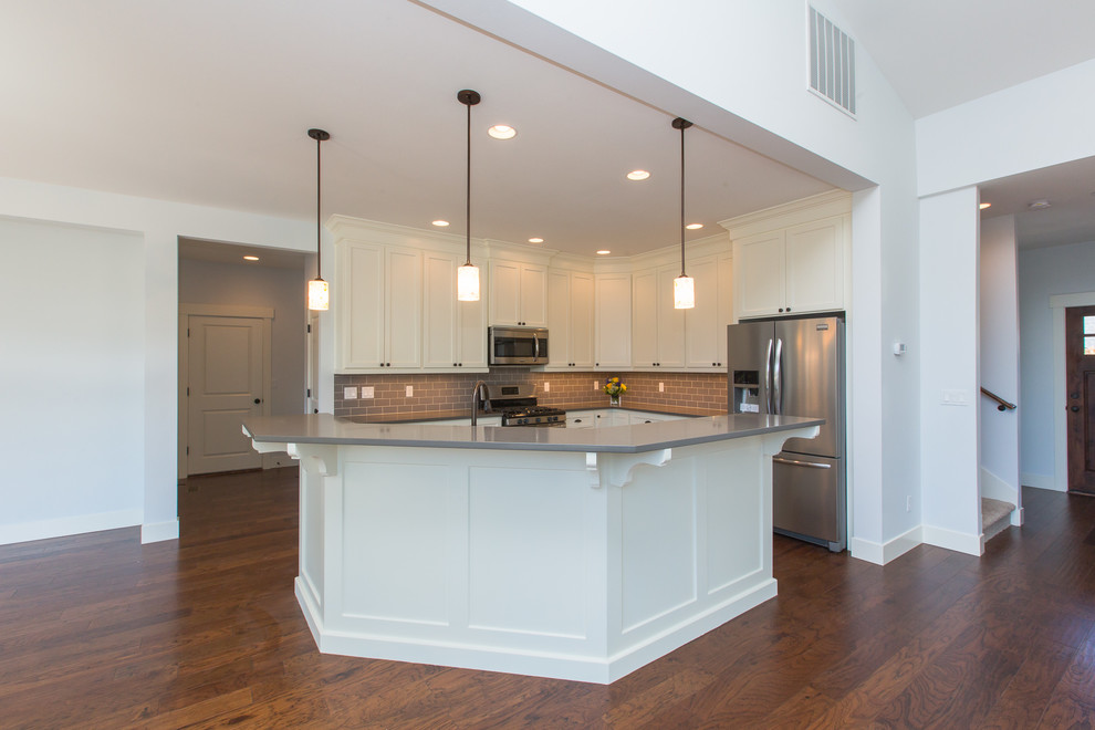 Inspiration for a large timeless u-shaped medium tone wood floor open concept kitchen remodel in Portland with a drop-in sink, shaker cabinets, white cabinets, quartzite countertops, gray backsplash, glass tile backsplash, stainless steel appliances and an island