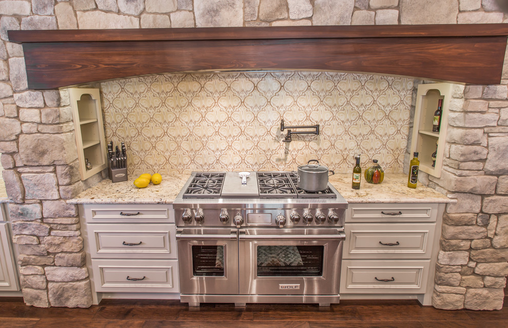 Example of a tuscan u-shaped dark wood floor and brown floor enclosed kitchen design in Jacksonville with an undermount sink, raised-panel cabinets, beige cabinets, granite countertops, white backsplash, mosaic tile backsplash, stainless steel appliances, an island and brown countertops