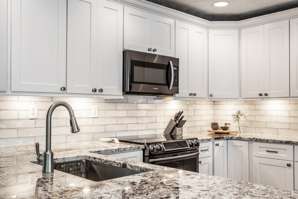 Example of a mid-sized minimalist u-shaped vinyl floor and brown floor eat-in kitchen design in Indianapolis with an undermount sink, shaker cabinets, white cabinets, quartz countertops, gray backsplash, ceramic backsplash, stainless steel appliances, an island and multicolored countertops