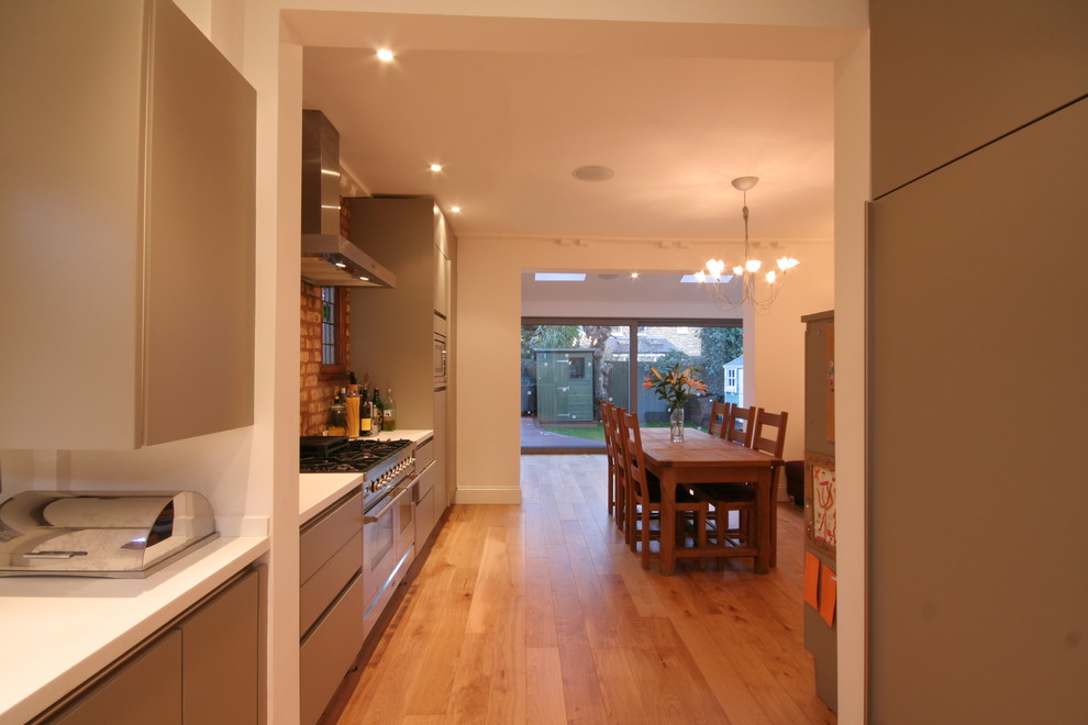 Stilmix Küche mit Landhausspüle, flächenbündigen Schrankfronten, grauen Schränken, Mineralwerkstoff-Arbeitsplatte, hellem Holzboden und weißer Arbeitsplatte in Gloucestershire