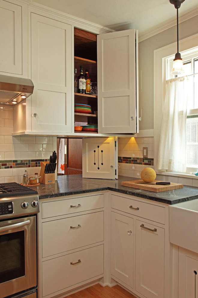Bild på ett litet amerikanskt kök, med en rustik diskho, luckor med infälld panel, vita skåp, flerfärgad stänkskydd, stänkskydd i mosaik, rostfria vitvaror, ljust trägolv, bänkskiva i täljsten och beiget golv