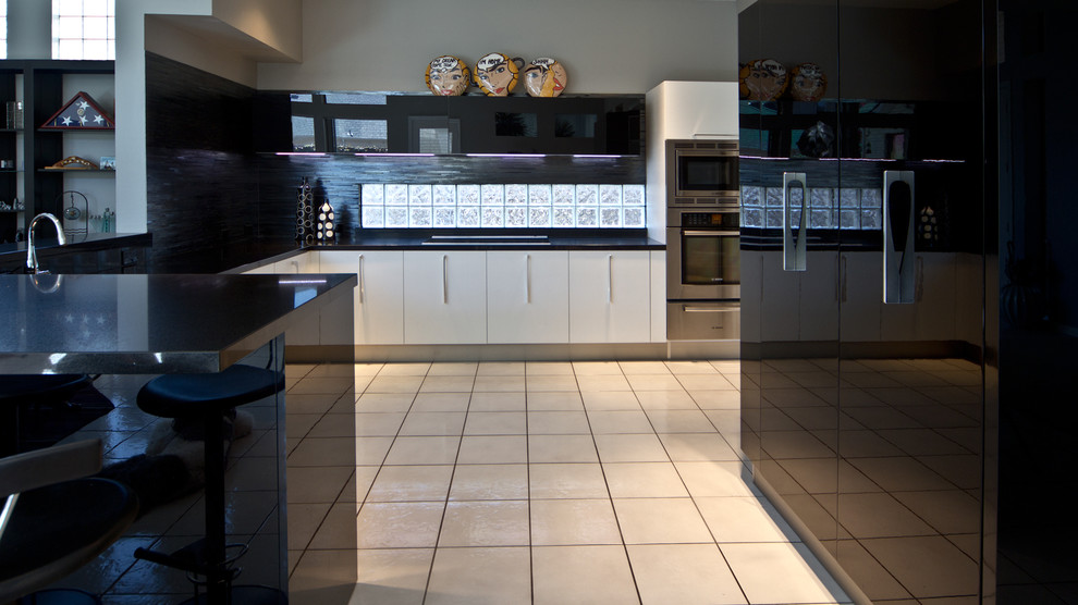 Diseño de cocina minimalista con armarios con paneles lisos, salpicadero negro, salpicadero de azulejos de vidrio y electrodomésticos de acero inoxidable
