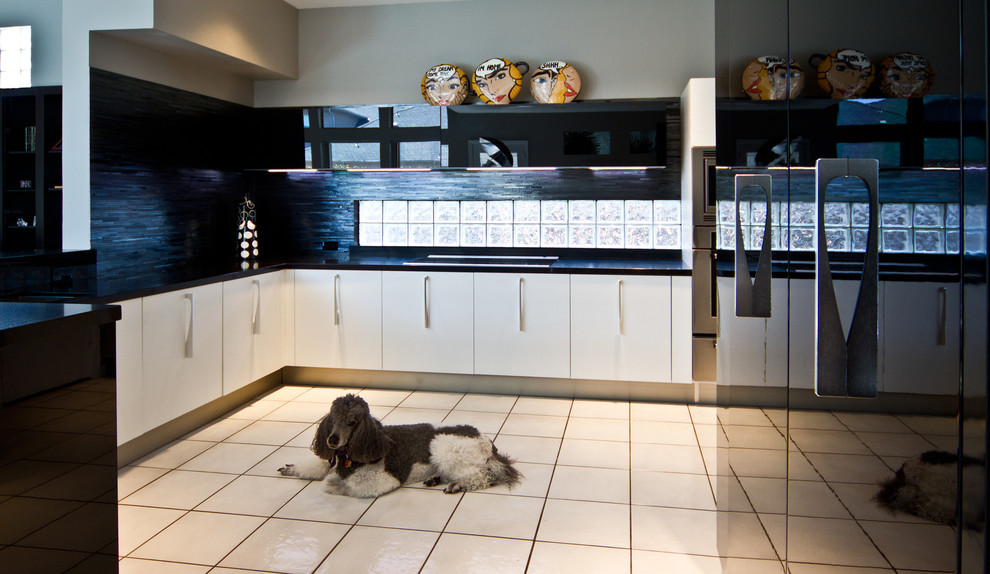 Diseño de cocina moderna con armarios con paneles lisos, salpicadero negro, salpicadero de azulejos de vidrio y electrodomésticos de acero inoxidable