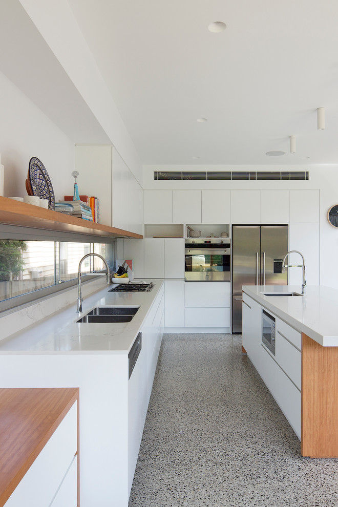 Immagine di una grande cucina design con lavello a doppia vasca, ante lisce, ante bianche, top in superficie solida, elettrodomestici in acciaio inossidabile e pavimento in cemento