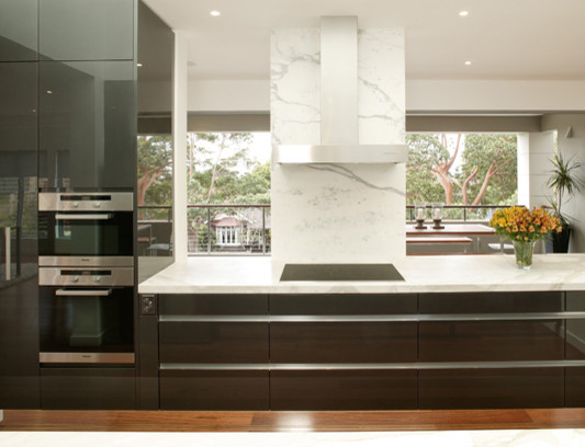 Modern inredning av ett mellanstort kök, med en undermonterad diskho, släta luckor, svarta skåp, marmorbänkskiva, vitt stänkskydd, rostfria vitvaror, mellanmörkt trägolv och en halv köksö