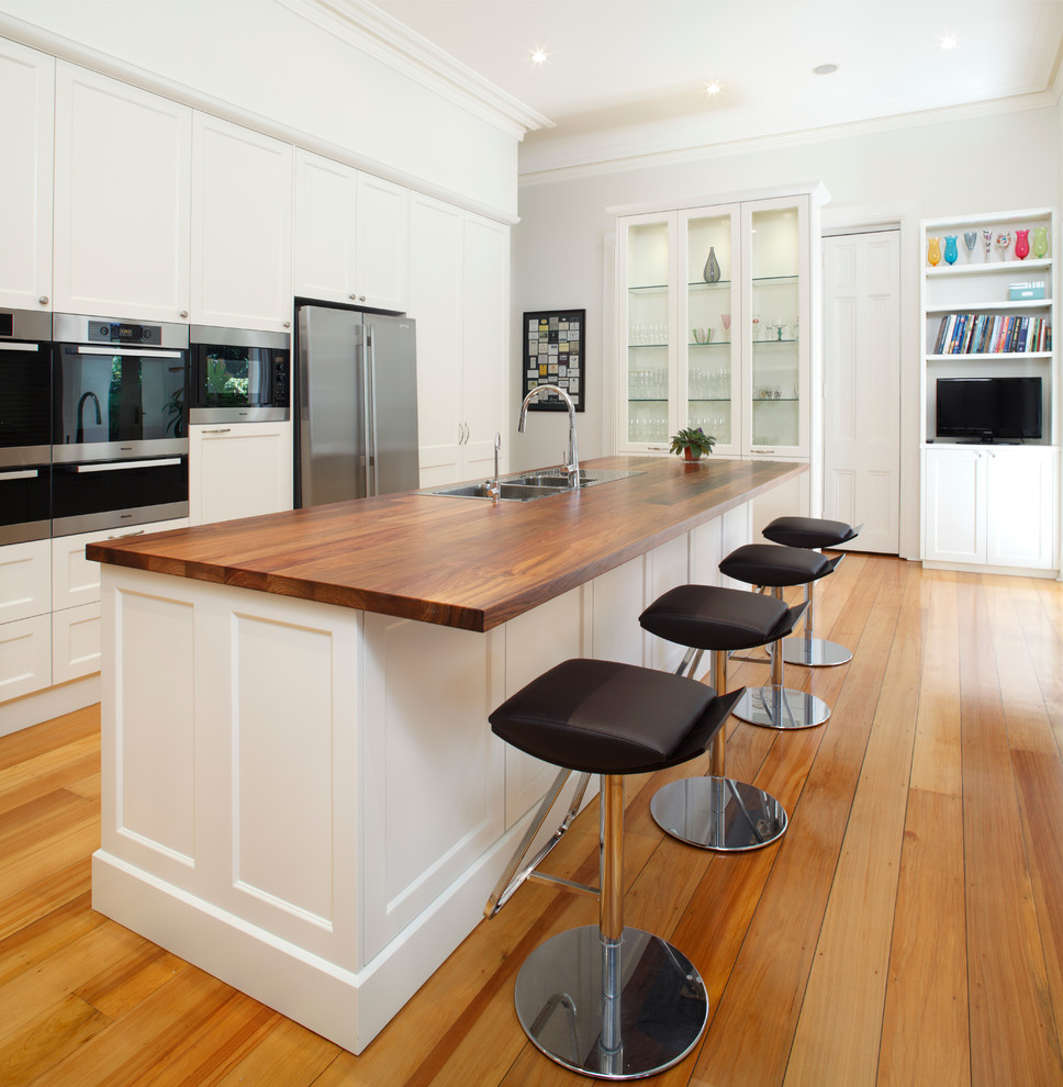 Mid-sized trendy galley medium tone wood floor eat-in kitchen photo in Sydney with a double-bowl sink, shaker cabinets, white cabinets, stainless steel appliances, wood countertops, multicolored backsplash, marble backsplash and an island