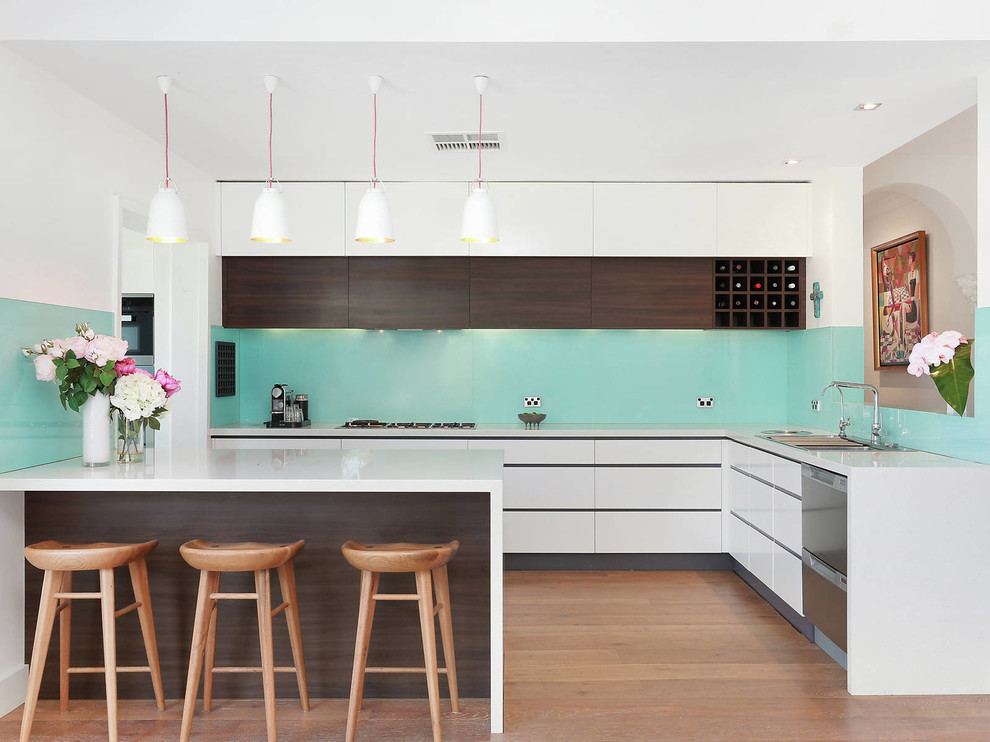 Große Moderne Küche in L-Form mit Küchengeräten aus Edelstahl, weißer Arbeitsplatte, Einbauwaschbecken, flächenbündigen Schrankfronten, weißen Schränken, Küchenrückwand in Blau, braunem Holzboden, Halbinsel und braunem Boden in Sydney