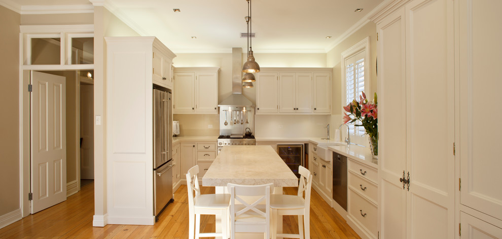 Example of a large transitional u-shaped medium tone wood floor open concept kitchen design in Sydney with a farmhouse sink, shaker cabinets, white cabinets, limestone countertops, white backsplash, glass sheet backsplash, stainless steel appliances and an island