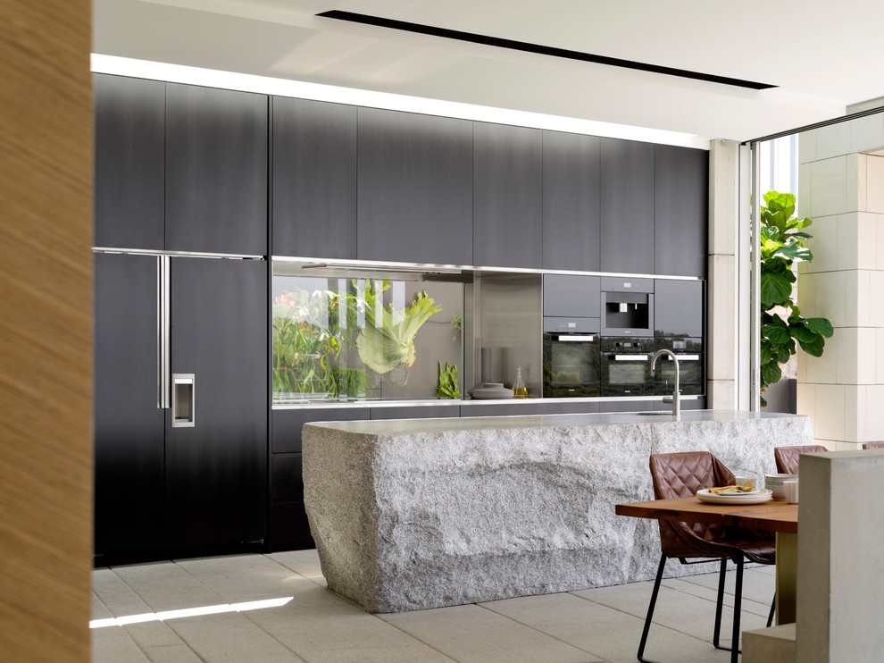 Imagen de cocina actual con encimera de vidrio, electrodomésticos negros, suelo de cemento y una isla