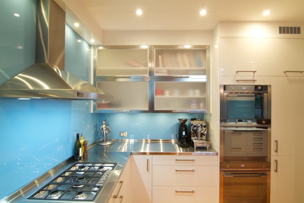Idee per una cucina minimalista chiusa e di medie dimensioni con lavello integrato, ante lisce, ante bianche, top in acciaio inossidabile, paraspruzzi blu, paraspruzzi con lastra di vetro, elettrodomestici in acciaio inossidabile, parquet chiaro e top bianco