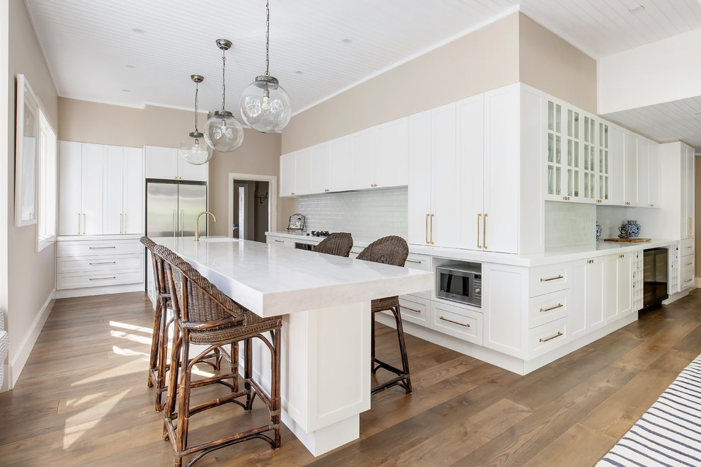 Idéer för ett mycket stort modernt vit kök, med en undermonterad diskho, skåp i shakerstil, vita skåp, bänkskiva i koppar, vitt stänkskydd, stänkskydd i tunnelbanekakel, rostfria vitvaror, mellanmörkt trägolv, en köksö och brunt golv