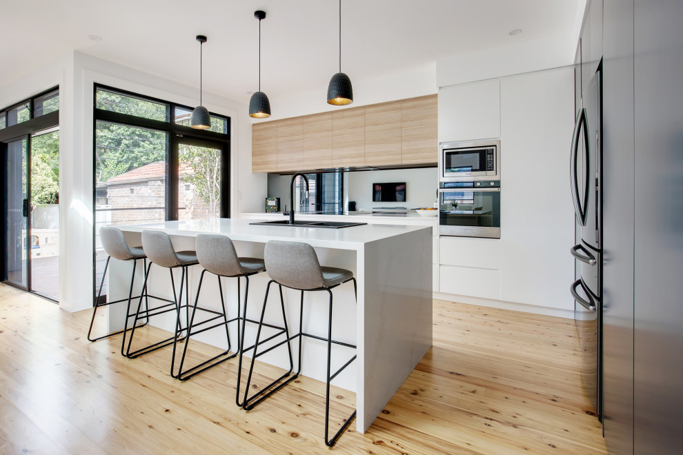 Inspiration for a mid-sized modern l-shaped light wood floor and multicolored floor open concept kitchen remodel in Sydney with a drop-in sink, flat-panel cabinets, quartz countertops, metallic backsplash, mirror backsplash, stainless steel appliances, an island and white countertops