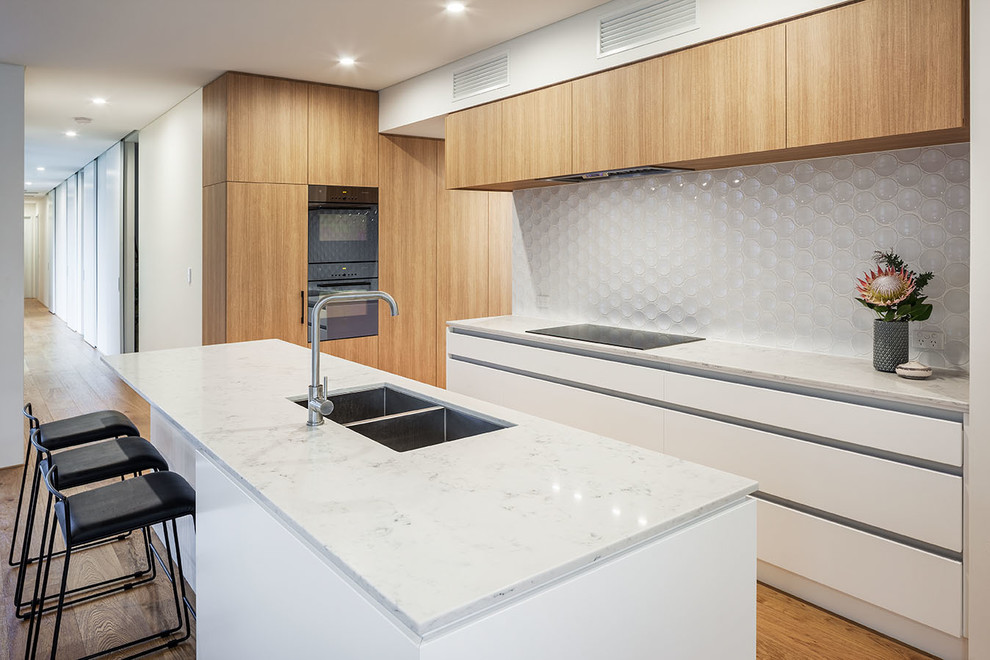 Immagine di una cucina nordica di medie dimensioni con lavello sottopiano, ante in legno chiaro, top in marmo, paraspruzzi bianco, paraspruzzi con piastrelle in ceramica e elettrodomestici neri