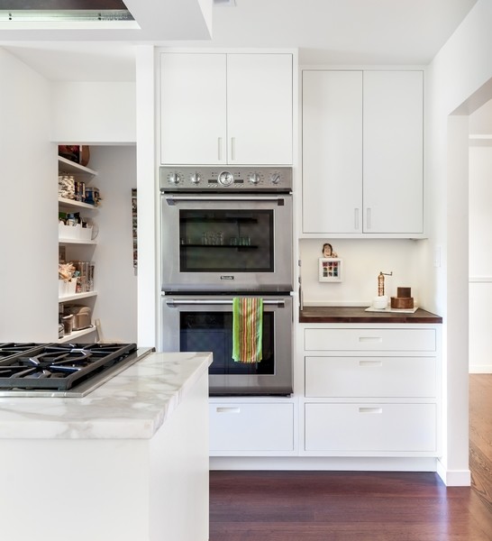 Photo of a medium sized modern u-shaped kitchen/diner in Sacramento with a built-in sink, recessed-panel cabinets, white cabinets, wood worktops, white splashback, integrated appliances, dark hardwood flooring and an island.