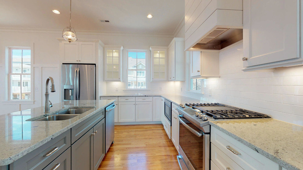 Eat-in kitchen - mid-sized coastal u-shaped light wood floor and brown floor eat-in kitchen idea in Raleigh with a double-bowl sink, shaker cabinets, white cabinets, quartzite countertops, white backsplash, ceramic backsplash, stainless steel appliances, an island and gray countertops