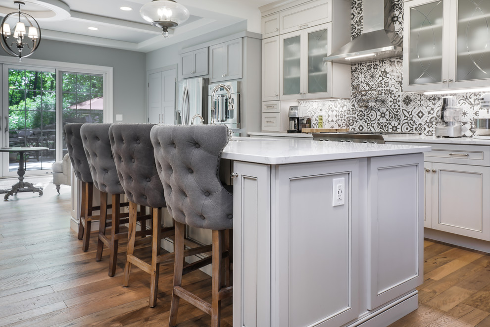 Open concept kitchen - mid-sized single-wall medium tone wood floor and brown floor open concept kitchen idea with an undermount sink, shaker cabinets, white cabinets, multicolored backsplash, stainless steel appliances, an island and white countertops