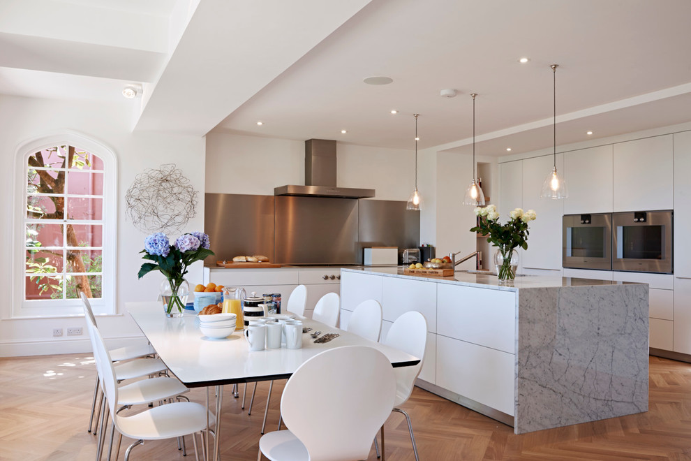 Imagen de cocina comedor contemporánea con armarios con paneles lisos, puertas de armario blancas, electrodomésticos de acero inoxidable, suelo de madera en tonos medios y una isla