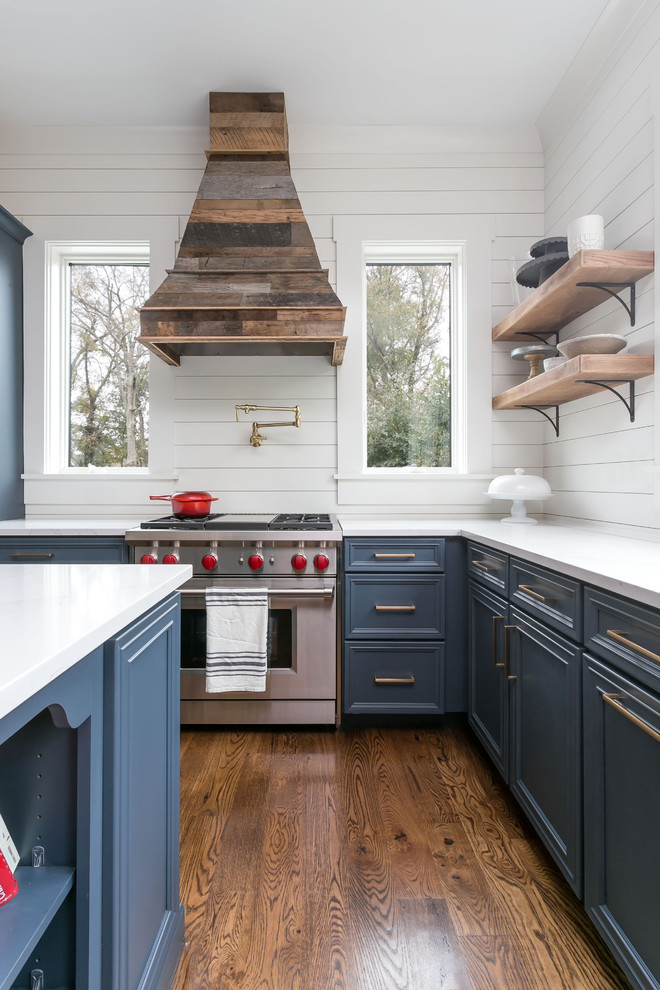 Bild på ett mellanstort maritimt vit vitt kök, med luckor med infälld panel, blå skåp, marmorbänkskiva, vitt stänkskydd, stänkskydd i trä, en köksö, brunt golv, rostfria vitvaror och mörkt trägolv