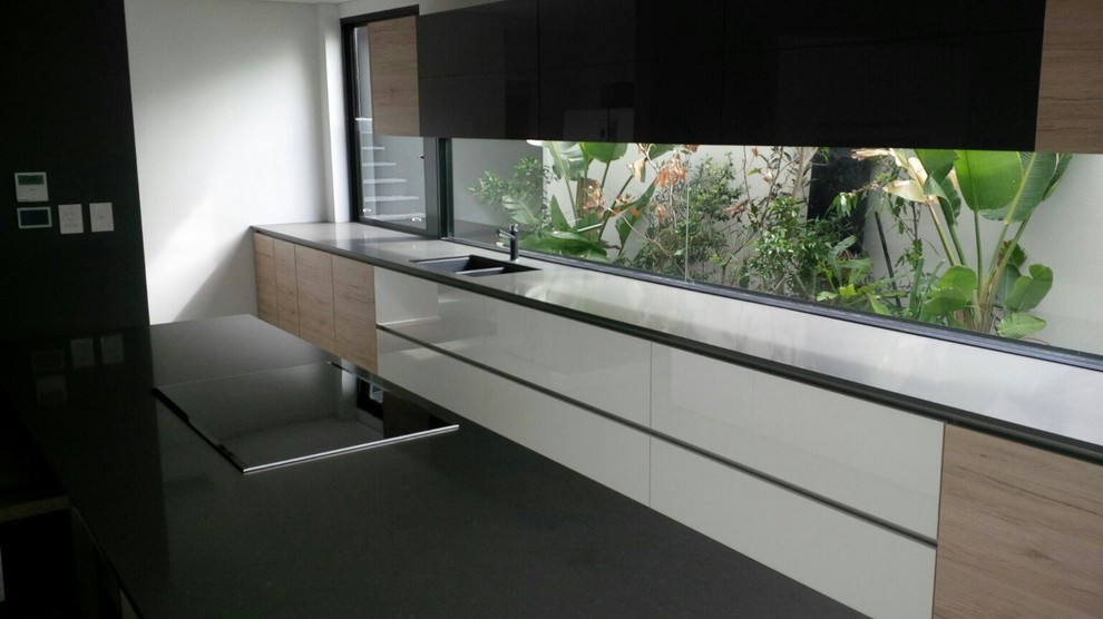 Foto di una grande cucina minimalista con lavello a doppia vasca, ante di vetro, ante in legno scuro, top in quarzo composito e elettrodomestici neri