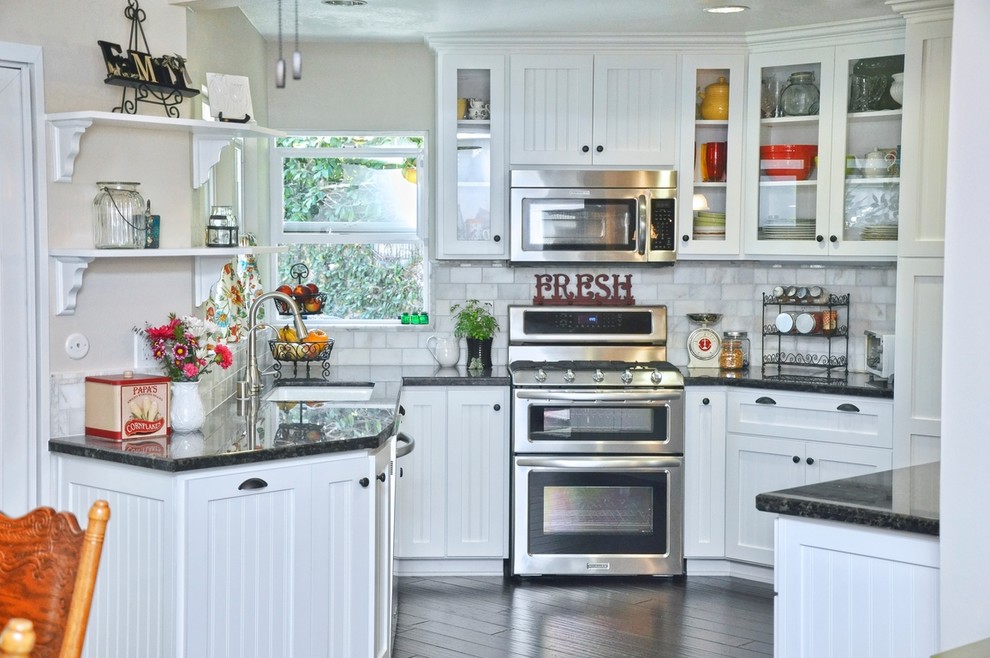 Inspiration for a small country u-shaped kitchen/diner in Los Angeles with a submerged sink, shaker cabinets, white cabinets, granite worktops, grey splashback, metro tiled splashback, stainless steel appliances, dark hardwood flooring, no island, brown floors and black worktops.