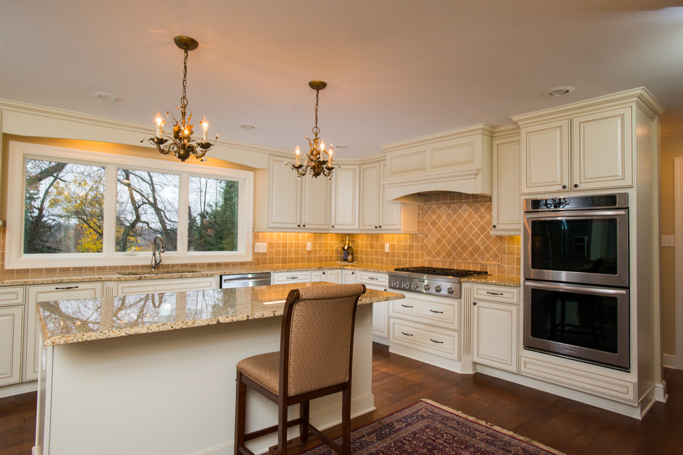 Inredning av ett klassiskt stort kök, med en undermonterad diskho, luckor med upphöjd panel, vita skåp, granitbänkskiva, beige stänkskydd, rostfria vitvaror, mörkt trägolv och en köksö