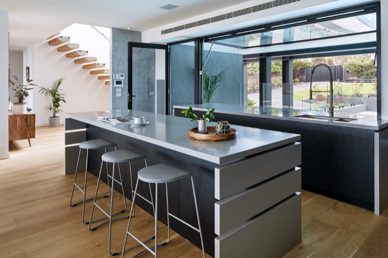 Immagine di un'ampia cucina minimal con ante nere, pavimento in legno massello medio, pavimento marrone, top grigio, ante lisce e elettrodomestici in acciaio inossidabile
