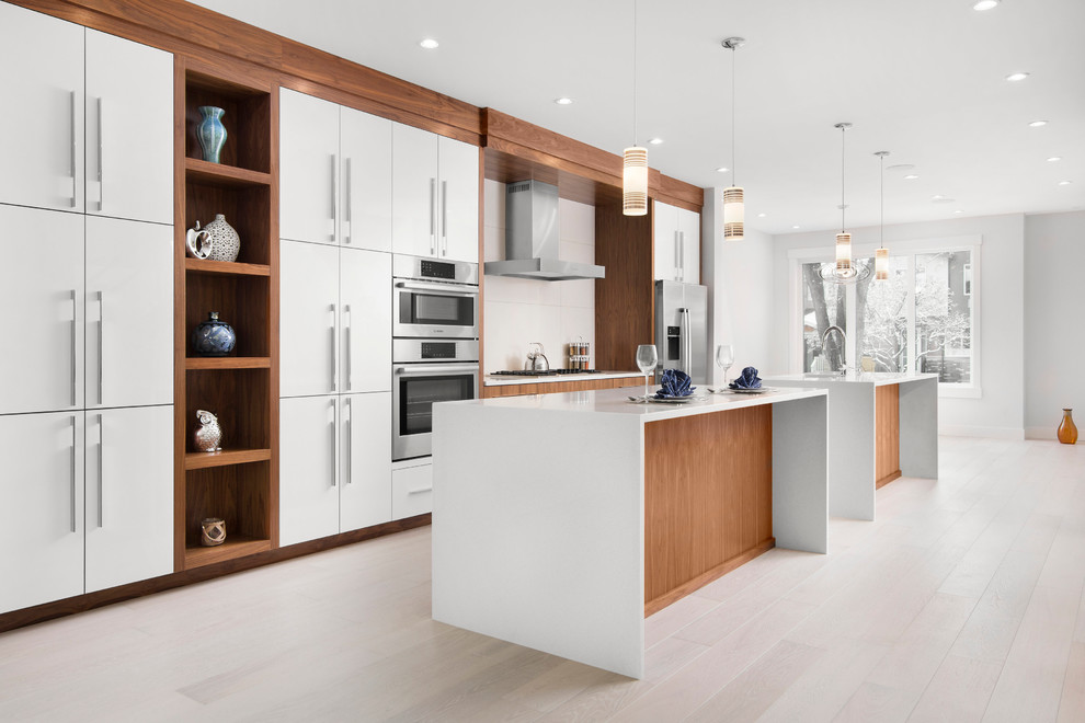 Photo of a medium sized contemporary galley open plan kitchen in Calgary with a double-bowl sink, flat-panel cabinets, medium wood cabinets, engineered stone countertops, white splashback, ceramic splashback, stainless steel appliances, light hardwood flooring and multiple islands.