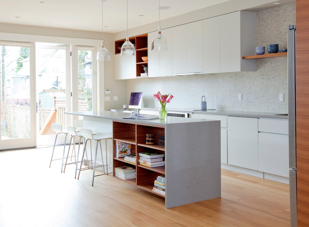 This is an example of a contemporary galley kitchen in Vancouver with flat-panel cabinets, white cabinets, white splashback, mosaic tiled splashback, light hardwood flooring and an island.