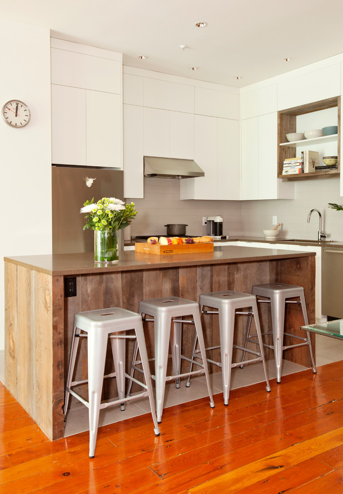 Mittelgroße Moderne Wohnküche in L-Form mit Unterbauwaschbecken, flächenbündigen Schrankfronten, weißen Schränken, Küchenrückwand in Weiß, Küchengeräten aus Edelstahl, braunem Holzboden und Kücheninsel in Vancouver