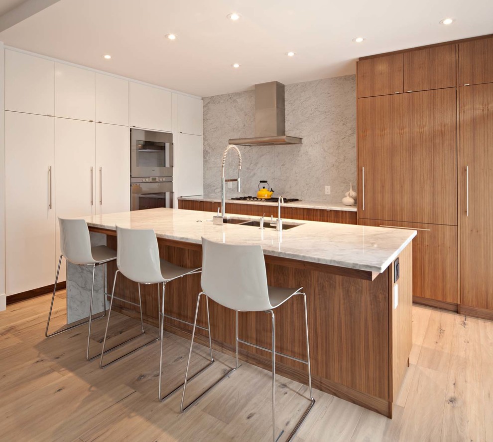 Design ideas for a medium sized modern single-wall open plan kitchen in Calgary with a submerged sink, flat-panel cabinets, beige cabinets, marble worktops, grey splashback, marble splashback, integrated appliances, light hardwood flooring, an island and beige floors.