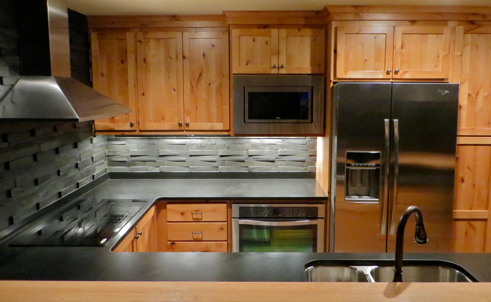 Inredning av ett rustikt litet kök, med en undermonterad diskho, luckor med infälld panel, skåp i mellenmörkt trä, granitbänkskiva, grått stänkskydd, stänkskydd i stenkakel, rostfria vitvaror, klinkergolv i porslin och en halv köksö