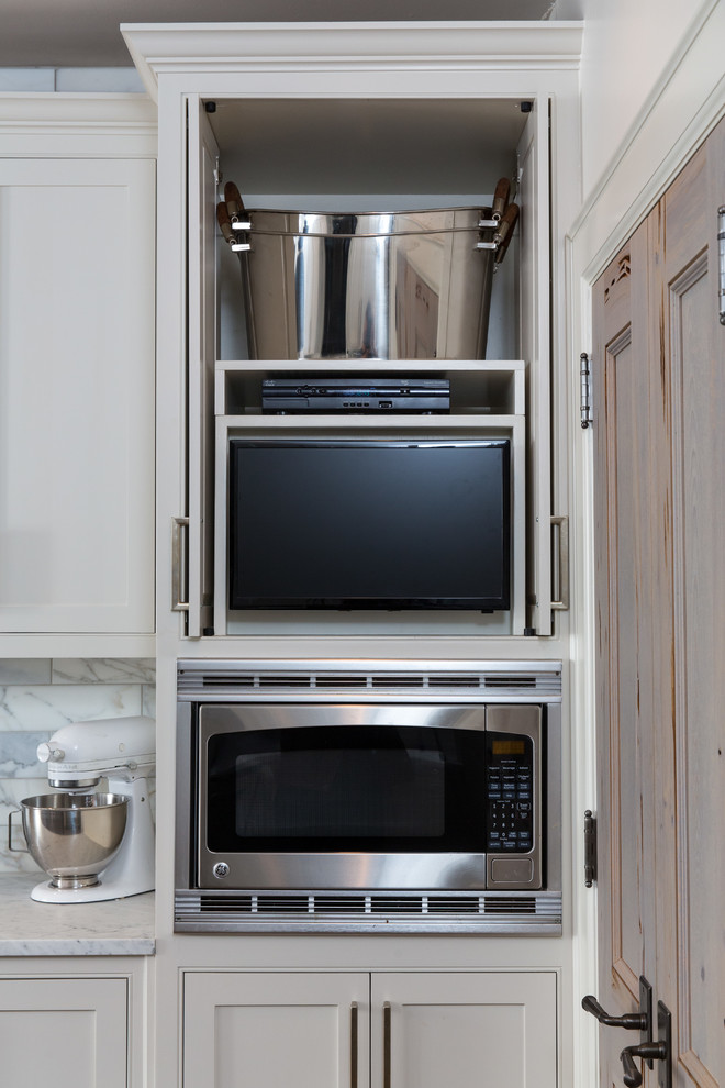 Cette photo montre une cuisine parallèle chic fermée avec des portes de placard blanches, un électroménager en acier inoxydable, un sol en bois brun et îlot.