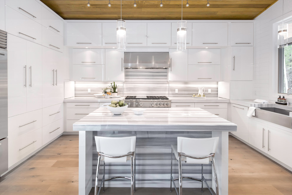 This is an example of a contemporary kitchen in Denver with a belfast sink, flat-panel cabinets, white cabinets, multi-coloured splashback, stainless steel appliances, light hardwood flooring, an island and beige floors.