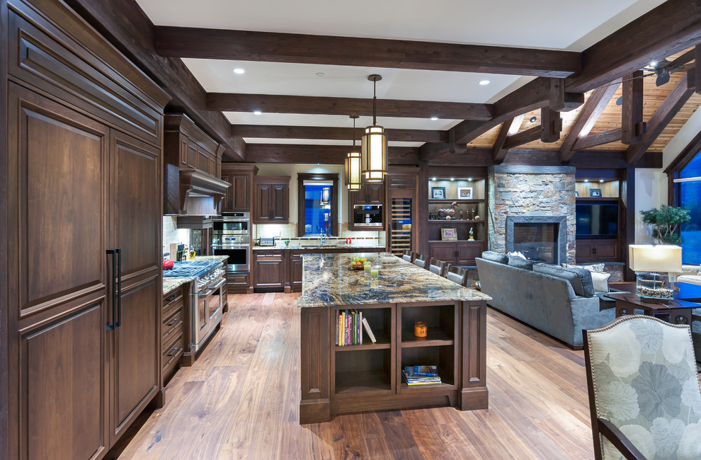 Bild på ett stort rustikt kök, med bruna skåp, mellanmörkt trägolv, brunt golv, en undermonterad diskho, luckor med upphöjd panel, granitbänkskiva, beige stänkskydd, stänkskydd i stenkakel, integrerade vitvaror och en köksö