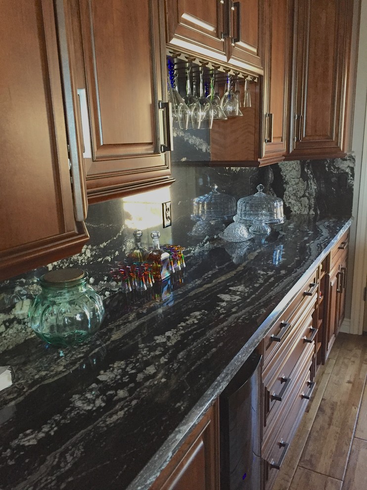 Urige Küche mit profilierten Schrankfronten, hellbraunen Holzschränken, Granit-Arbeitsplatte, Küchenrückwand in Schwarz und Rückwand aus Stein in Phoenix