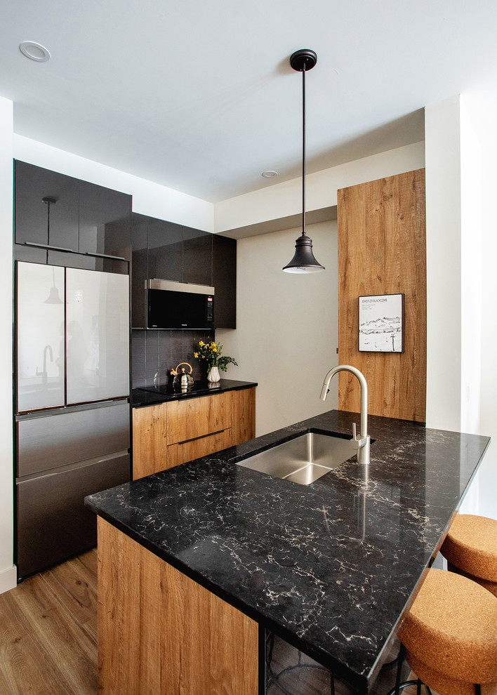 Small trendy galley laminate floor and brown floor kitchen photo in Toronto with flat-panel cabinets, quartz countertops, subway tile backsplash, a peninsula, black countertops, an undermount sink, medium tone wood cabinets, gray backsplash and stainless steel appliances