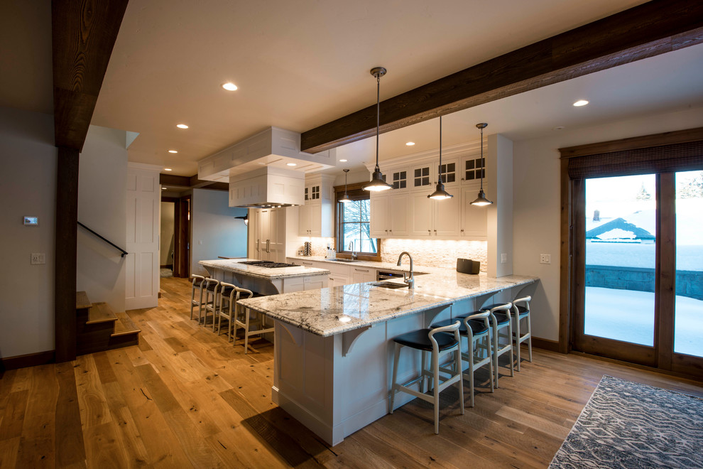 Eat-in kitchen - large rustic u-shaped light wood floor eat-in kitchen idea in Other with a drop-in sink, raised-panel cabinets, white cabinets, granite countertops, beige backsplash, stone tile backsplash, stainless steel appliances and an island