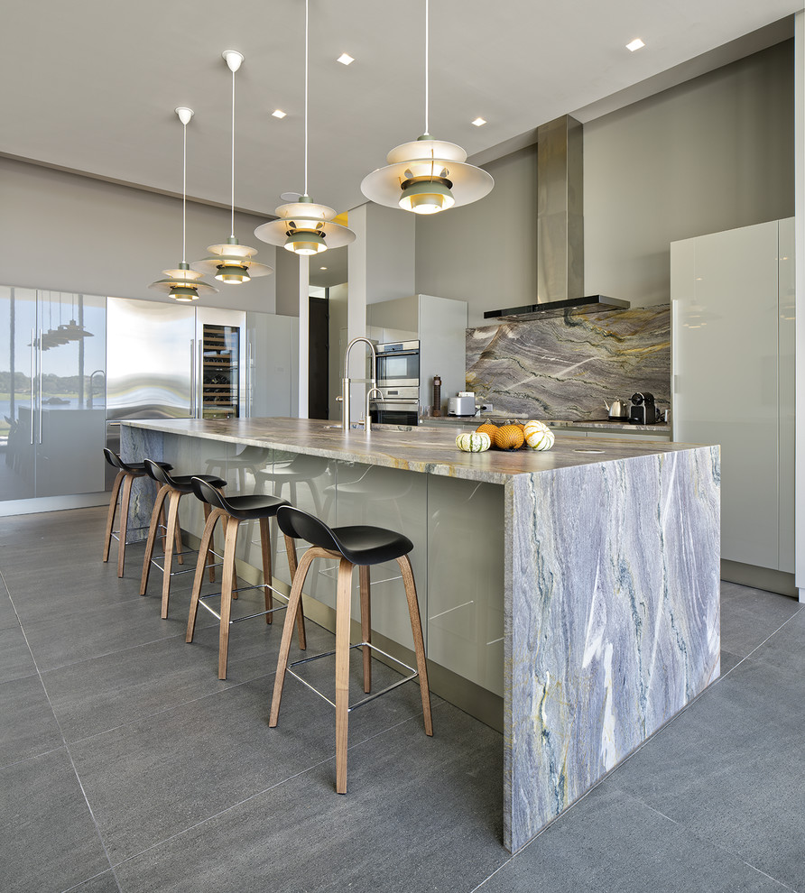 This is an example of a contemporary kitchen in Tampa with flat-panel cabinets, grey cabinets, stone slab splashback, stainless steel appliances, an island and grey floors.