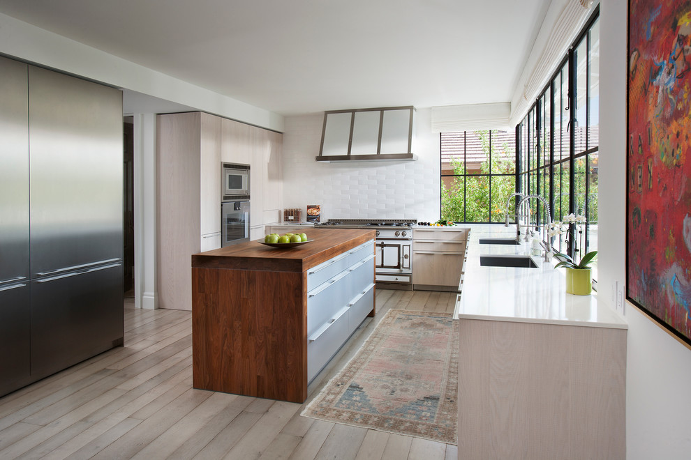 Klassische Küche in L-Form mit Unterbauwaschbecken, flächenbündigen Schrankfronten, hellen Holzschränken, Küchenrückwand in Weiß, hellem Holzboden und Kücheninsel in Los Angeles