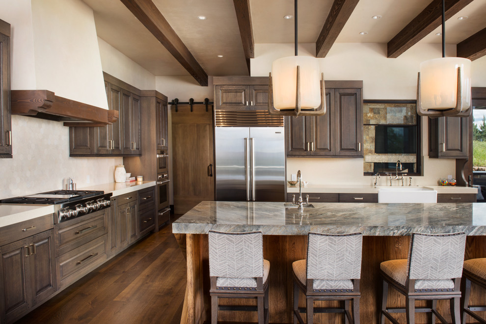 Kitchen pantry - huge transitional l-shaped medium tone wood floor and brown floor kitchen pantry idea in Denver with a farmhouse sink, raised-panel cabinets, medium tone wood cabinets, quartzite countertops, beige backsplash, stone tile backsplash, stainless steel appliances and an island