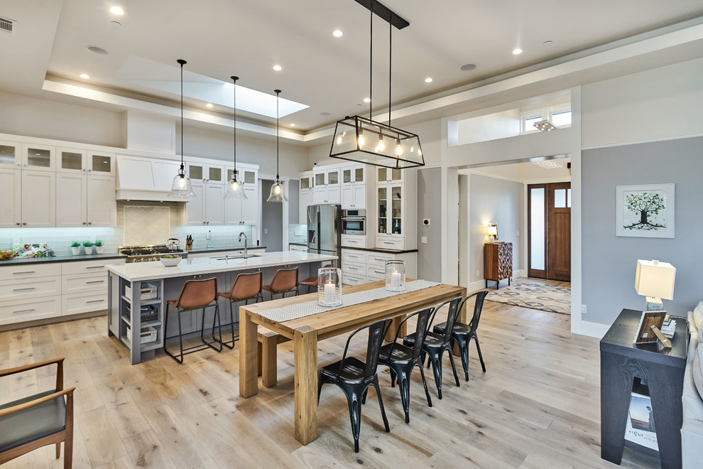 Traditional galley open plan kitchen in San Francisco with shaker cabinets, white cabinets, blue splashback, glass tiled splashback, stainless steel appliances, light hardwood flooring, an island and beige floors.