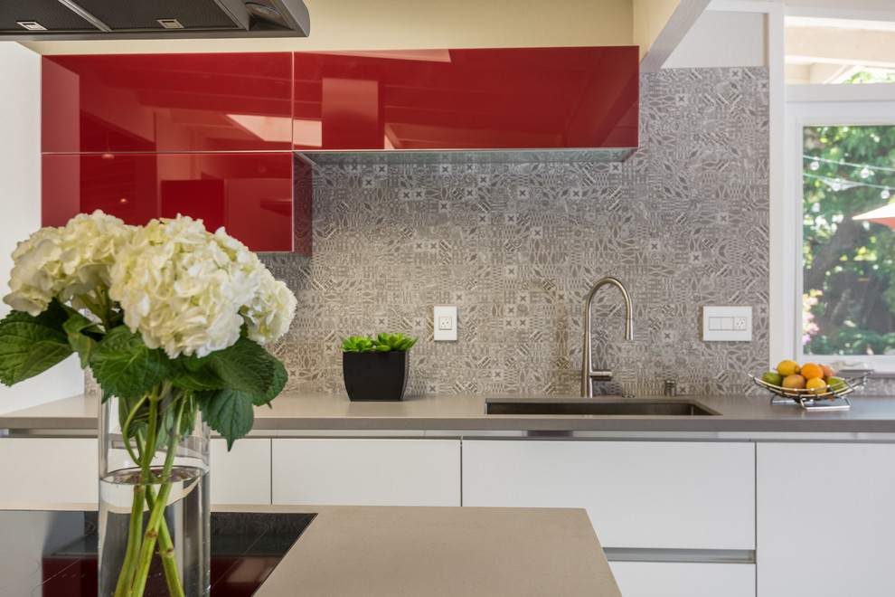 Photo of a medium sized modern galley enclosed kitchen in San Francisco with a submerged sink, flat-panel cabinets, red cabinets, engineered stone countertops, grey splashback, ceramic splashback, stainless steel appliances, ceramic flooring, an island, grey floors and grey worktops.